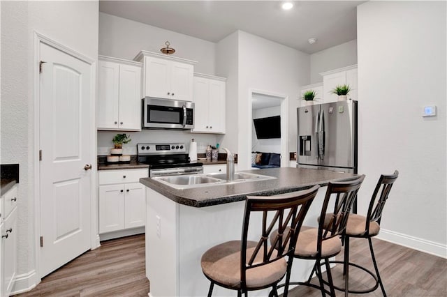 kitchen with stainless steel appliances, dark countertops, a kitchen island with sink, and white cabinetry