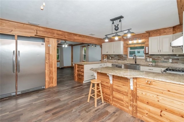 kitchen with light stone counters, stainless steel refrigerator, sink, and white cabinetry