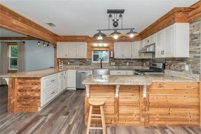 kitchen with decorative light fixtures, appliances with stainless steel finishes, light stone countertops, white cabinetry, and kitchen peninsula