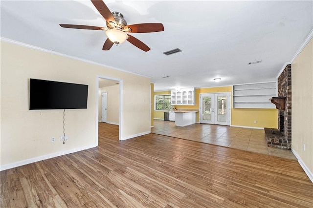 unfurnished living room featuring french doors, a brick fireplace, ornamental molding, hardwood / wood-style flooring, and ceiling fan