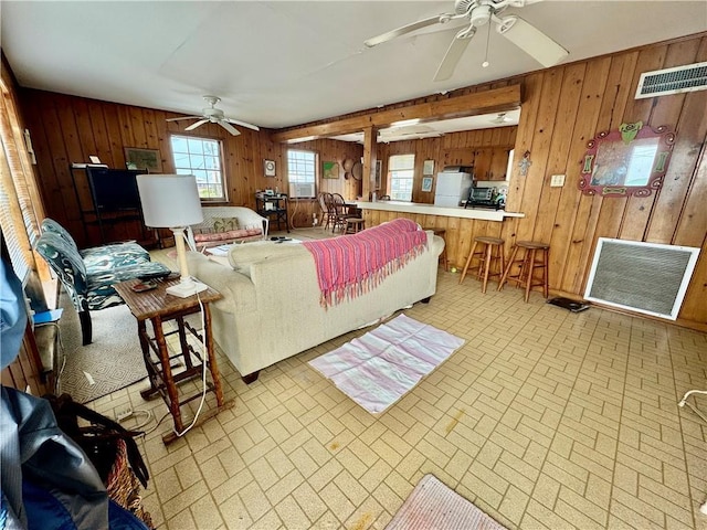 living area with visible vents, brick patterned floor, wooden walls, and ceiling fan