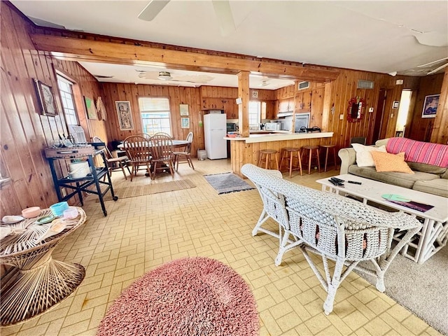 living area featuring brick patterned floor, beam ceiling, and wood walls