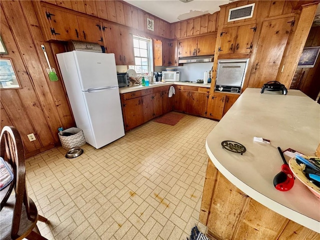 kitchen featuring white appliances, wooden walls, brown cabinets, and light countertops