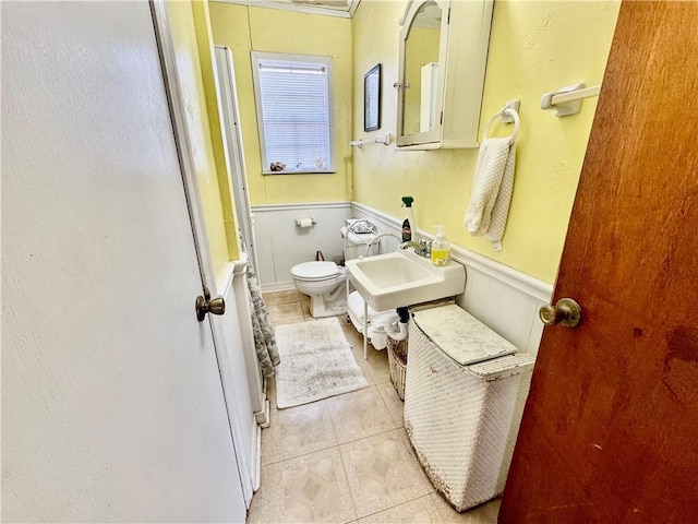 full bathroom featuring tile patterned floors, a wainscoted wall, toilet, and a sink