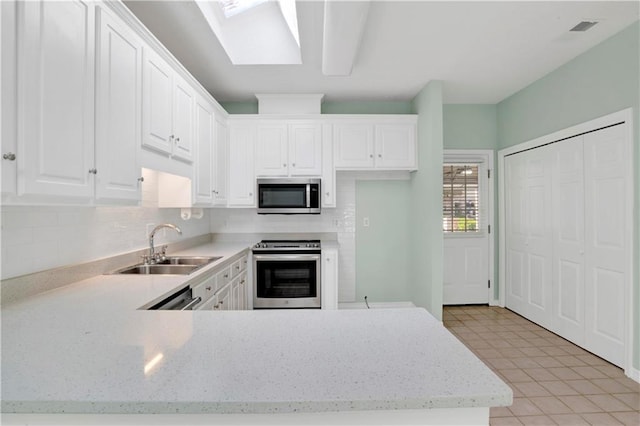 kitchen featuring appliances with stainless steel finishes, a skylight, sink, white cabinets, and light tile patterned floors