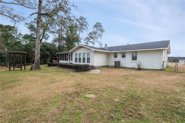 rear view of property with cooling unit, a sunroom, and a lawn