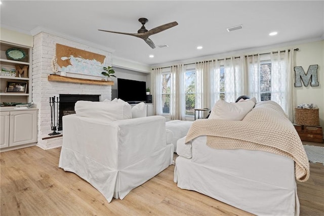 living room featuring crown molding, a brick fireplace, ceiling fan, and light wood-type flooring