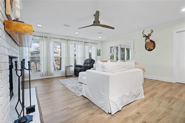 living room featuring a brick fireplace, crown molding, ceiling fan, and light wood-type flooring