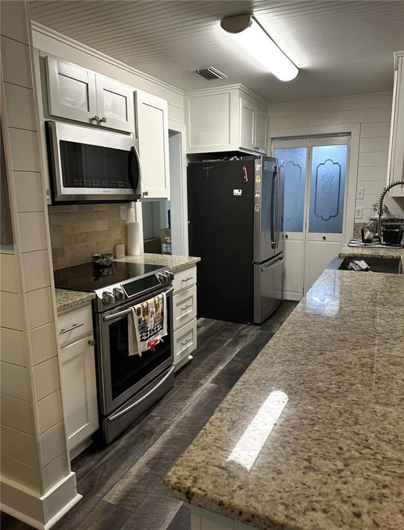 2911 Thornhill Dr, Mobile, AL 36606 - kitchen with appliances with stainless steel finishes, dark wood finished floors, light stone countertops, white cabinets, and tasteful backsplash