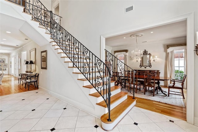 staircase with a notable chandelier, crown molding, hardwood / wood-style floors, and a high ceiling