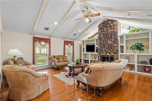 living room with built in features, a wealth of natural light, lofted ceiling with beams, light hardwood / wood-style floors, and a stone fireplace