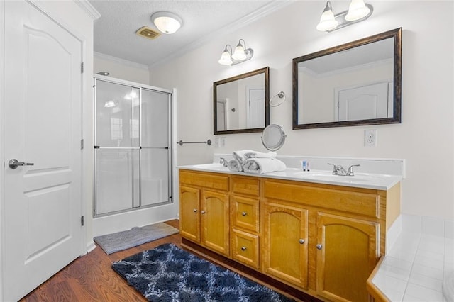 bathroom with vanity, a textured ceiling, wood-type flooring, crown molding, and an enclosed shower