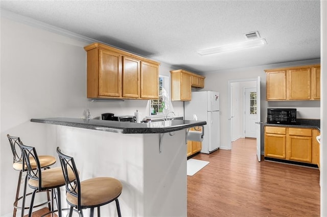 kitchen with a breakfast bar, a textured ceiling, kitchen peninsula, white fridge, and light hardwood / wood-style flooring