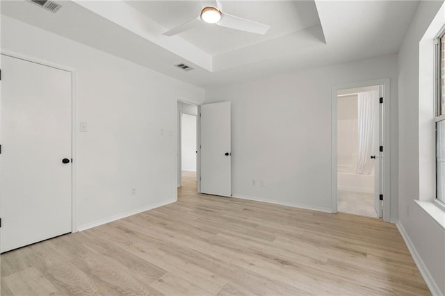 unfurnished bedroom with a tray ceiling, visible vents, and light wood-style flooring