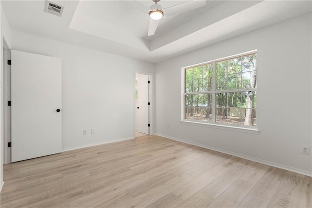unfurnished bedroom with baseboards, light wood finished floors, a tray ceiling, and visible vents