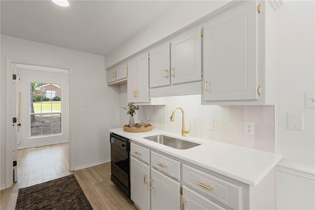 kitchen with black dishwasher, tasteful backsplash, light wood-type flooring, and a sink