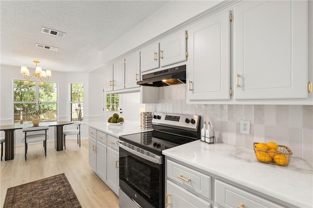 kitchen with under cabinet range hood, an inviting chandelier, visible vents, and electric range