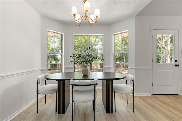 dining space with light wood finished floors, a textured ceiling, a healthy amount of sunlight, and a notable chandelier