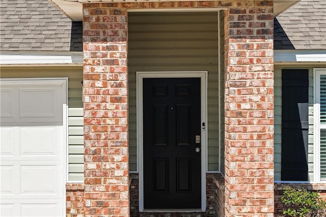 entrance to property with a shingled roof, brick siding, and a garage