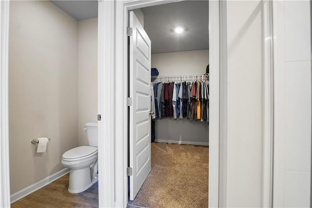 bathroom featuring toilet, a spacious closet, and baseboards