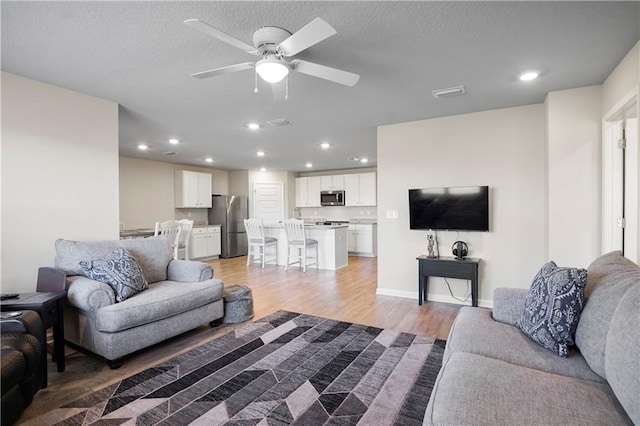 living room featuring a ceiling fan, recessed lighting, light wood-style flooring, and baseboards