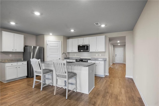 kitchen with appliances with stainless steel finishes, wood finished floors, visible vents, and white cabinets