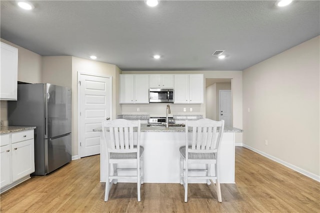 kitchen with stainless steel appliances, visible vents, white cabinetry, light wood finished floors, and a center island with sink