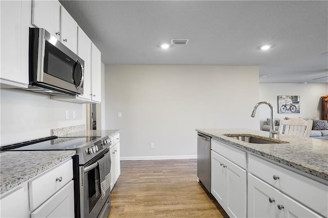 kitchen featuring light wood finished floors, stainless steel appliances, visible vents, white cabinetry, and a sink