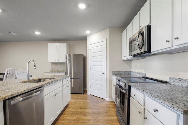 kitchen with stainless steel appliances, light wood-style floors, white cabinetry, a sink, and recessed lighting