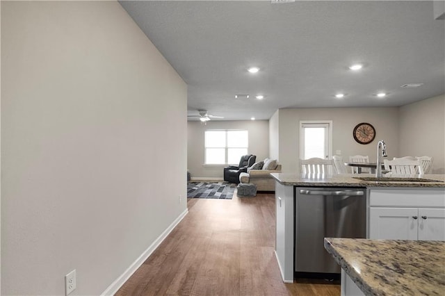 kitchen featuring light stone counters, stainless steel dishwasher, white cabinetry, a sink, and wood finished floors