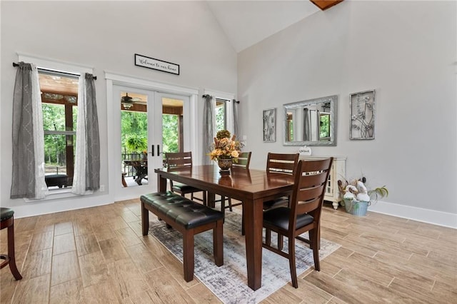 dining space with light wood-style floors, high vaulted ceiling, baseboards, and french doors