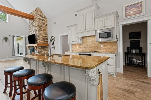 kitchen with decorative backsplash, a kitchen breakfast bar, a sink, light stone counters, and stainless steel microwave