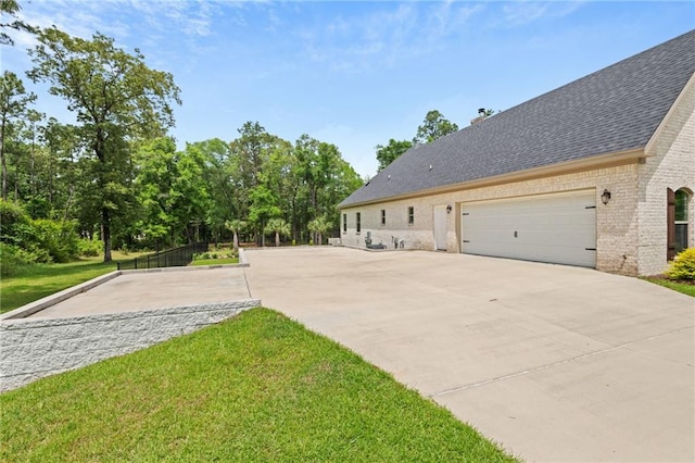 view of side of home featuring driveway, a chimney, roof with shingles, brick siding, and a yard