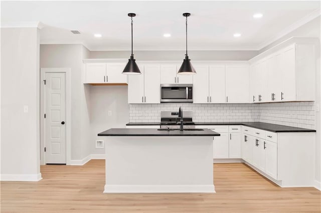 kitchen featuring dark countertops, a sink, stainless steel microwave, light wood-style floors, and white cabinetry