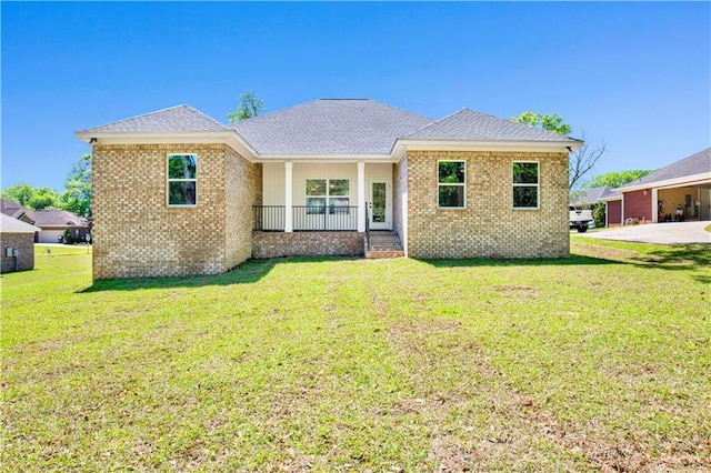 view of front of home with covered porch, brick siding, a front yard, and roof with shingles
