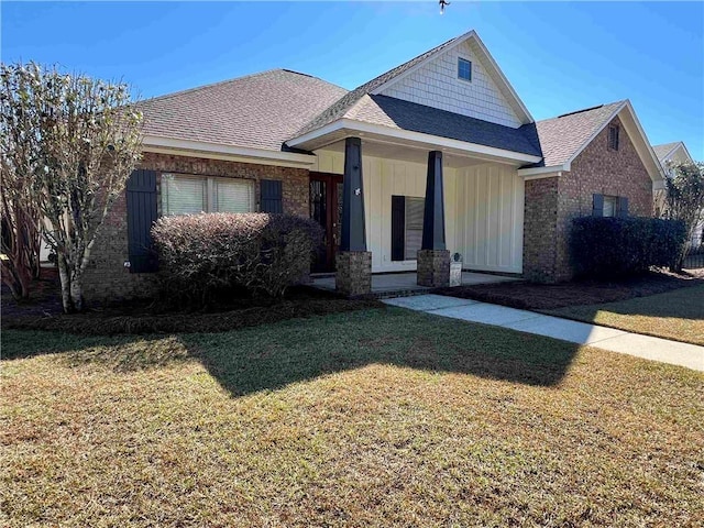 view of front of house featuring brick siding, a front yard, and a shingled roof