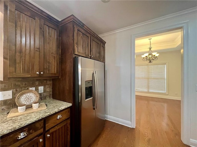 kitchen with light wood-type flooring, crown molding, stainless steel fridge with ice dispenser, and light stone countertops