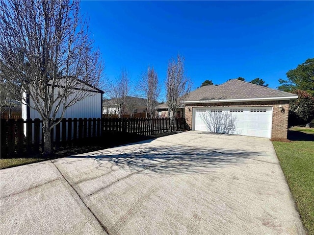 view of property exterior featuring concrete driveway, brick siding, a shingled roof, and fence