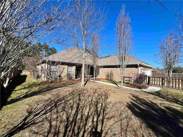 back of house with brick siding, fence, an attached garage, and a lawn