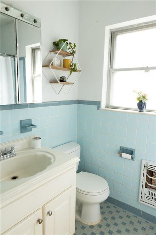 bathroom featuring vanity, toilet, heating unit, and tile walls