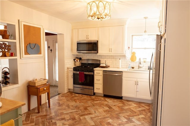 kitchen with sink, tasteful backsplash, appliances with stainless steel finishes, pendant lighting, and white cabinets