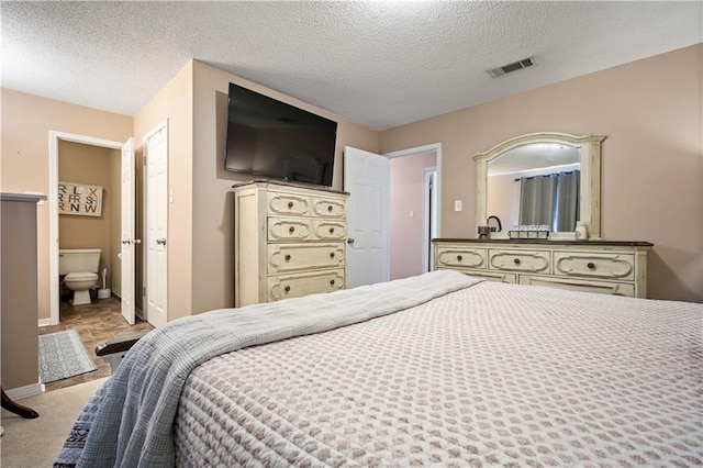 bedroom featuring a textured ceiling, light colored carpet, and ensuite bathroom