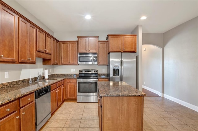 kitchen with arched walkways, a kitchen island, stainless steel appliances, a sink, and light tile patterned flooring