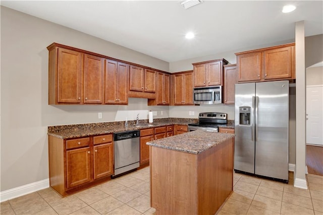 kitchen featuring appliances with stainless steel finishes, dark stone countertops, a sink, and brown cabinets