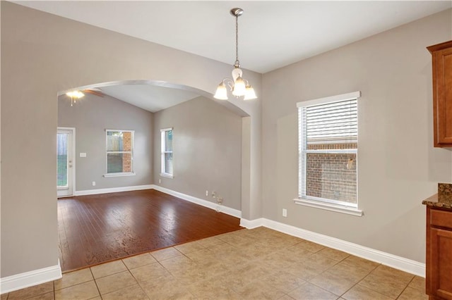 spare room with arched walkways, light tile patterned floors, an inviting chandelier, and baseboards