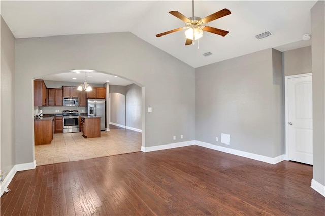 unfurnished living room with arched walkways, visible vents, a ceiling fan, wood finished floors, and baseboards