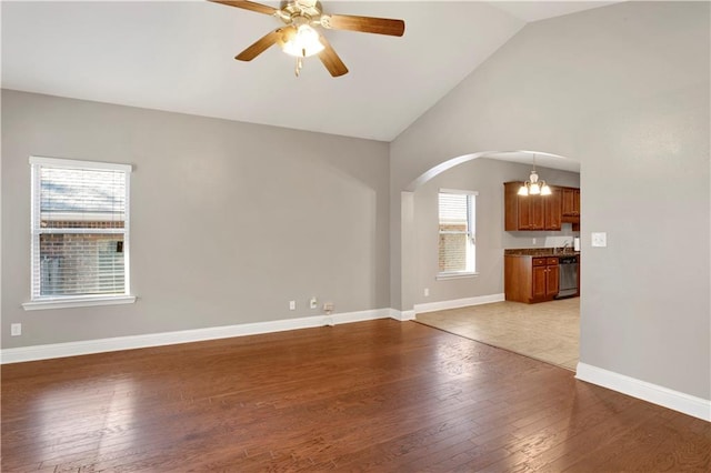 unfurnished living room featuring arched walkways, lofted ceiling, light wood-style flooring, a ceiling fan, and baseboards