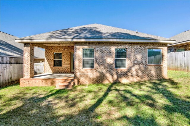 back of house with a patio, a fenced backyard, roof with shingles, a yard, and brick siding