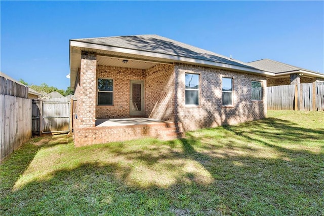 back of house featuring a yard, a fenced backyard, brick siding, and a patio