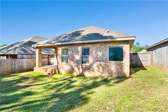 back of property with a yard, brick siding, roof with shingles, and a fenced backyard